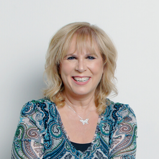 Headshot of Coach Suzanne, smiling, wearing a blue-toned paisley shirt with a small silver butterfly necklace